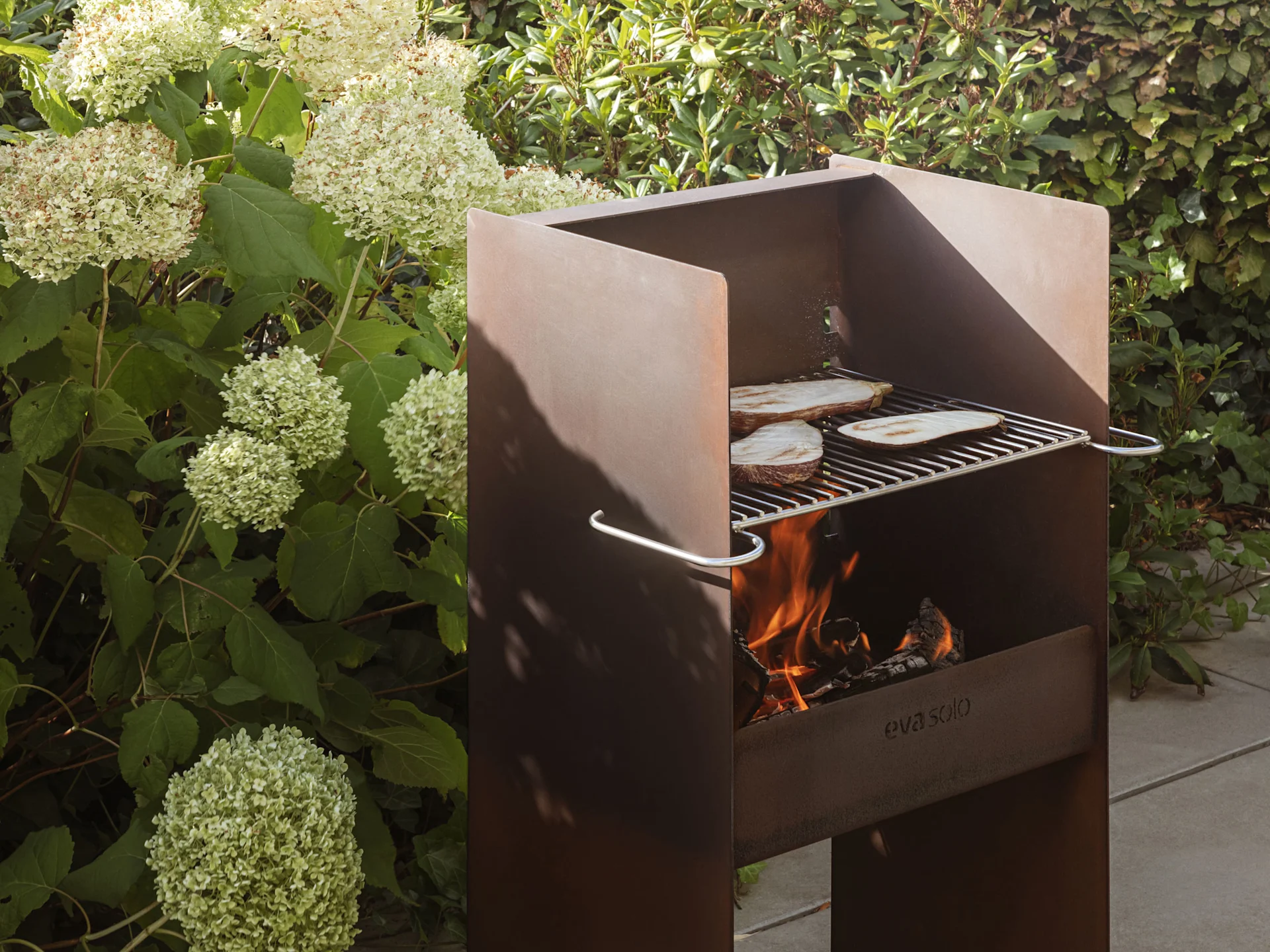 Um grelhador rústico de metal para exterior com chamas e fatias de beringela a cozinhar na grelha.