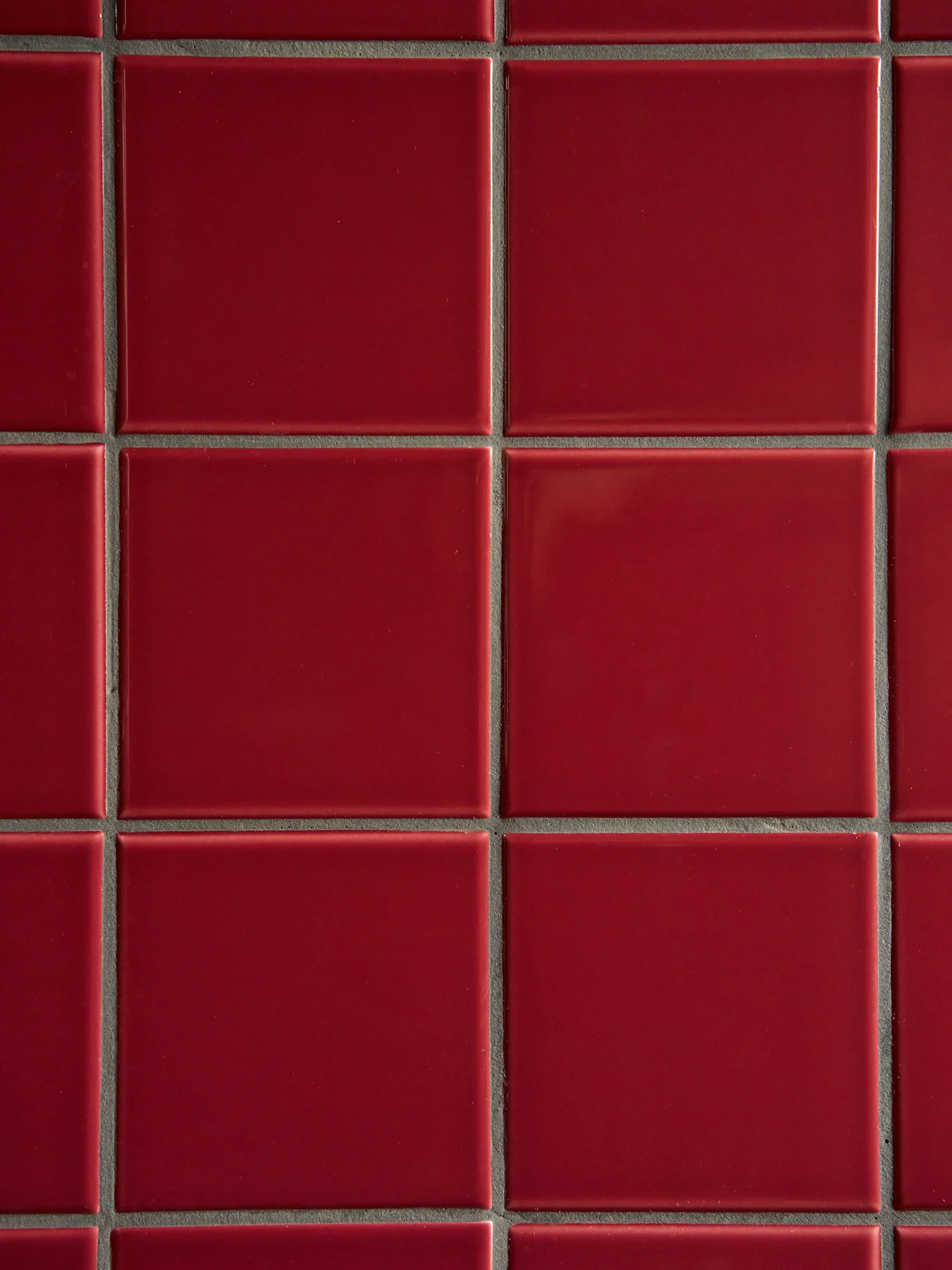 Uma grade de azulejos vermelhos quadrados e brilhantes com argamassa cinza escura.