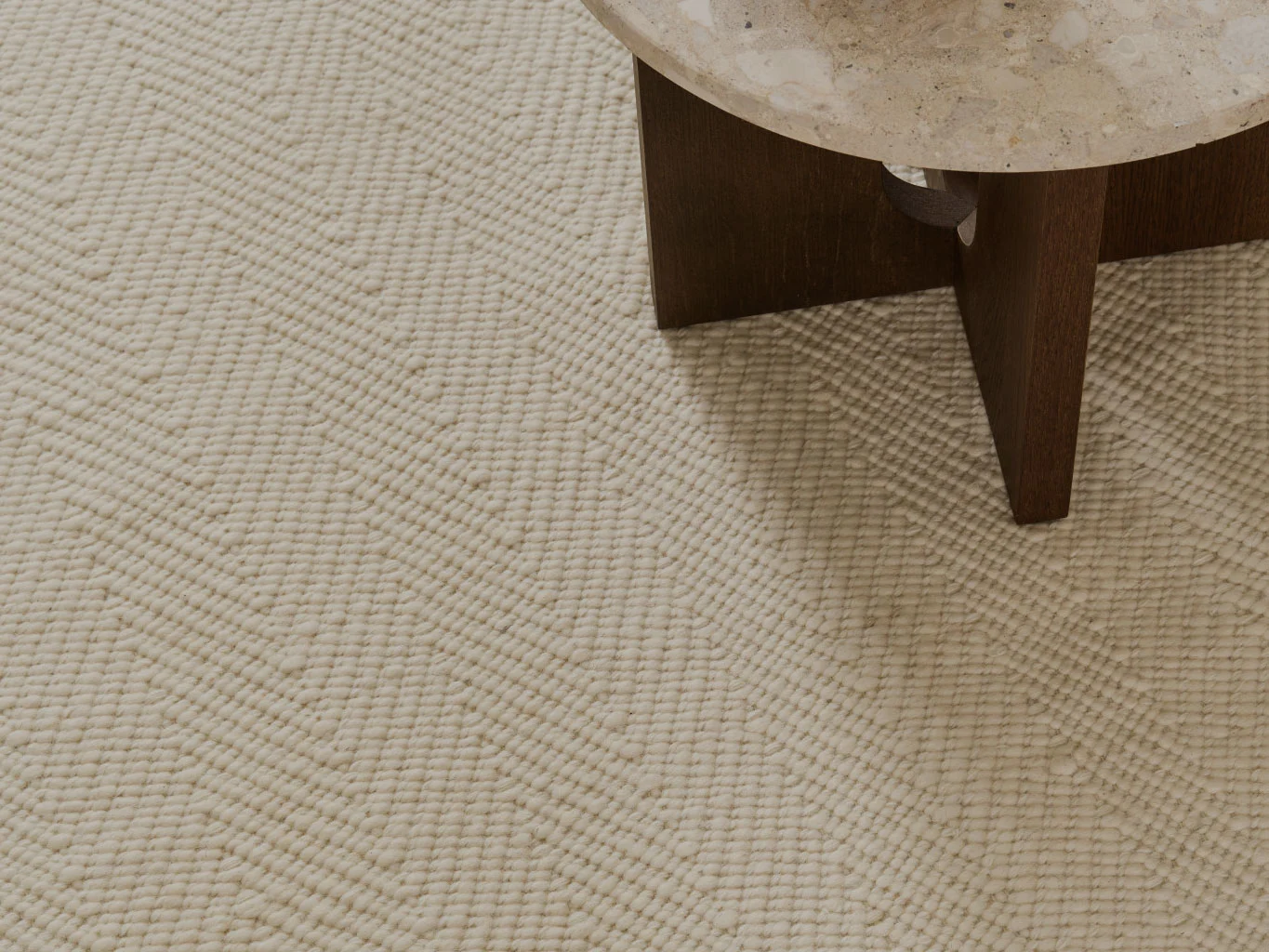 Close-up de um tapete texturizado cor creme com padrão em chevron, ao lado de uma mesa com tampo de pedra.