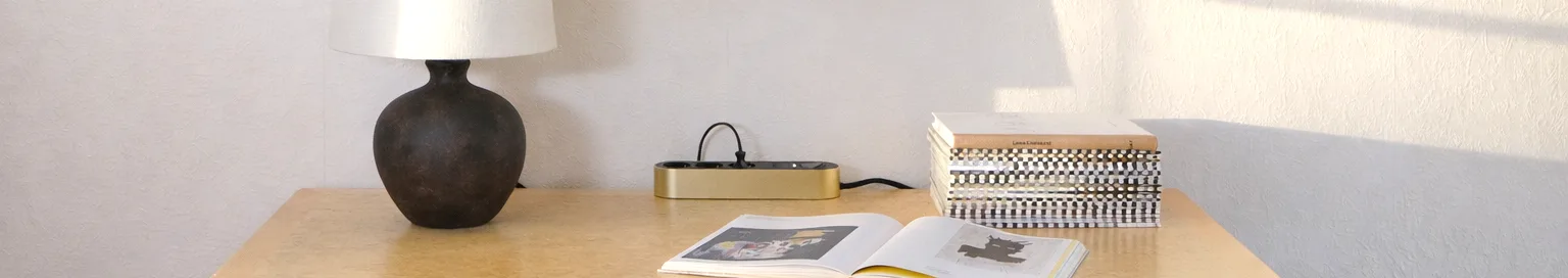 Extensão dourada com três tomadas pretas e um botão de ligar/desligar numa superfície clara.