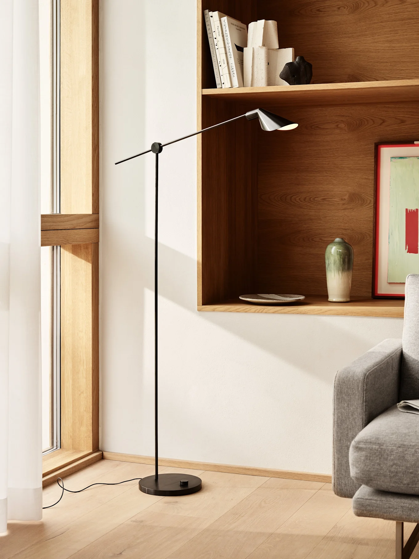 Candeeiro de pé preto alto e esguio com braço ajustável e abajur escuro numa sala de estar moderna com prateleiras de madeira.
