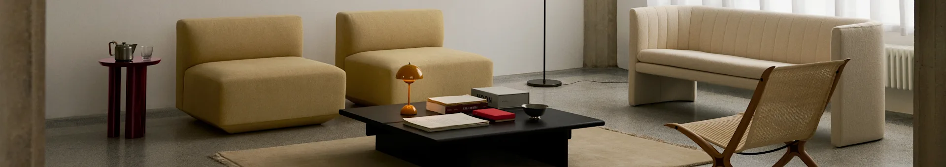 Uma sala de estar moderna com duas cadeiras mostarda sem braços, uma mesa de centro preta, um sofá canelado creme e uma cadeira de madeira tecida.