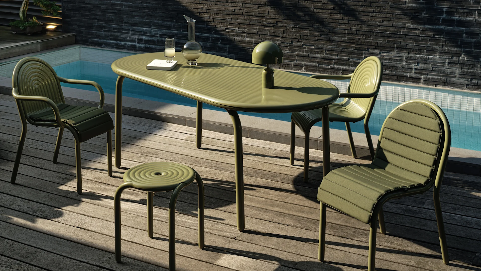 Conjunto de jantar exterior verde suave com mesa oval, três cadeiras almofadadas e um banco num deck de madeira junto a uma piscina. Um candeeiro, jarra e copo na mesa.