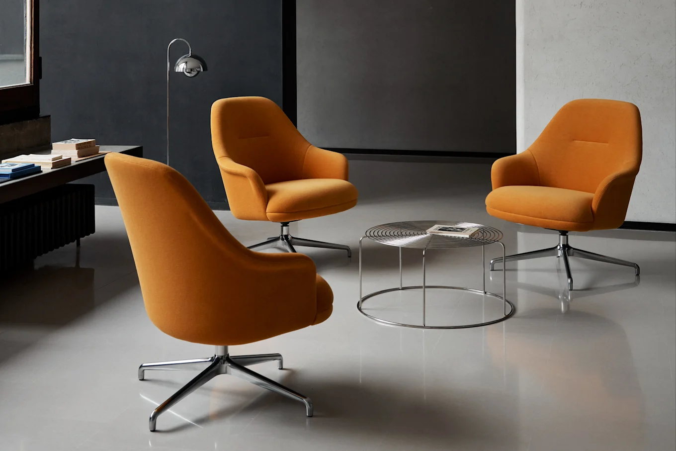 Três poltronas giratórias laranja dispostas em torno de uma mesa de centro redonda cromada em uma sala moderna.