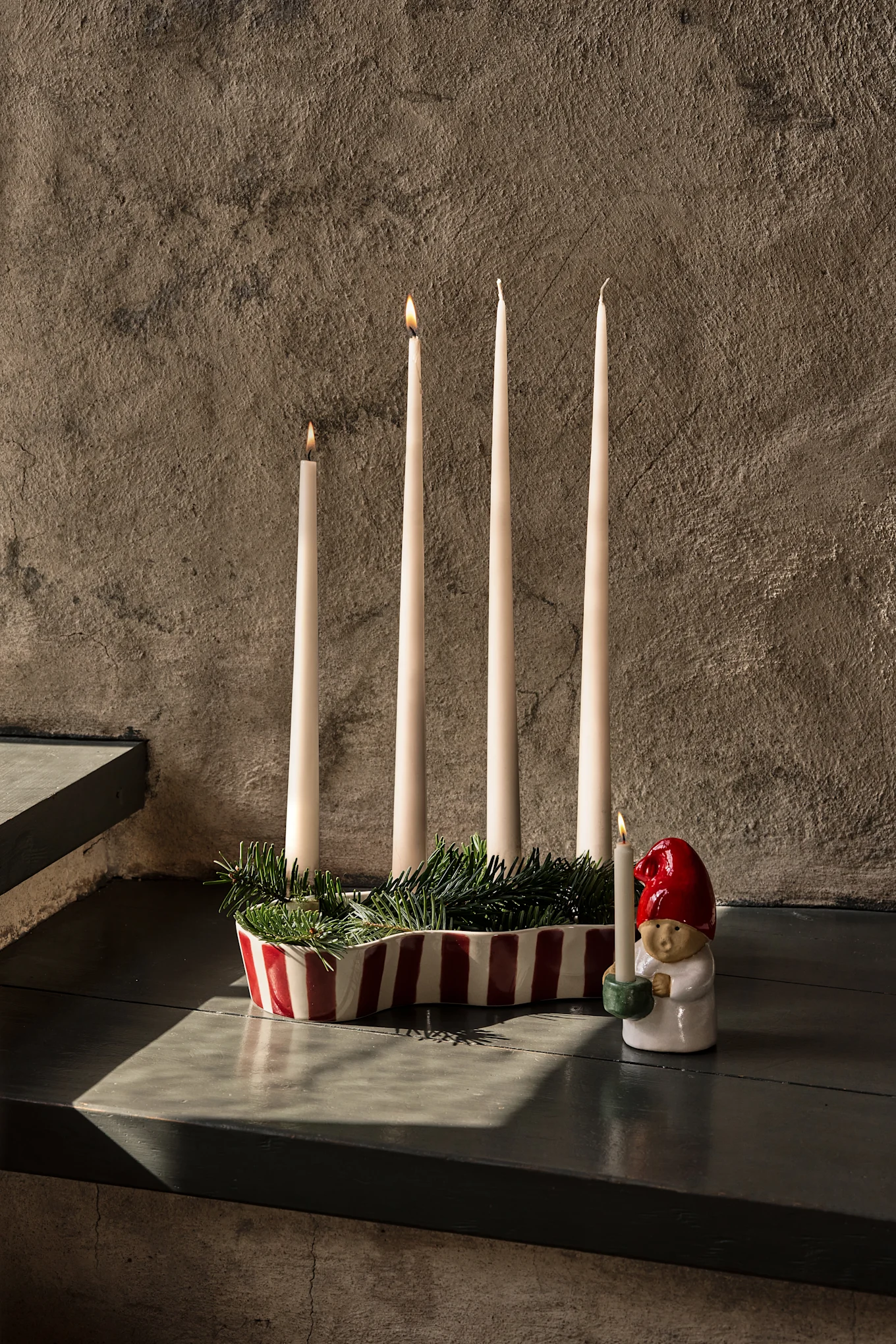 Mesa elegante posta com toalha vermelho-escura, copos de vinho, pratos, um suporte de frutas em camadas e velas acesas.