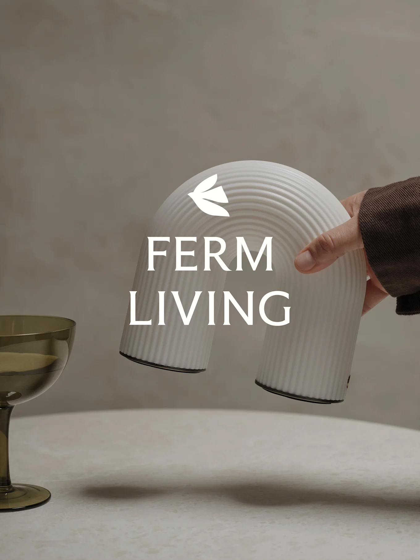 Mão segurando um objeto decorativo branco canelado em forma de arco, com um copo verde próximo.