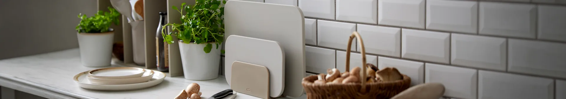 Duas tábuas de corte bege num suporte sobre um balcão de cozinha com outros utensílios.