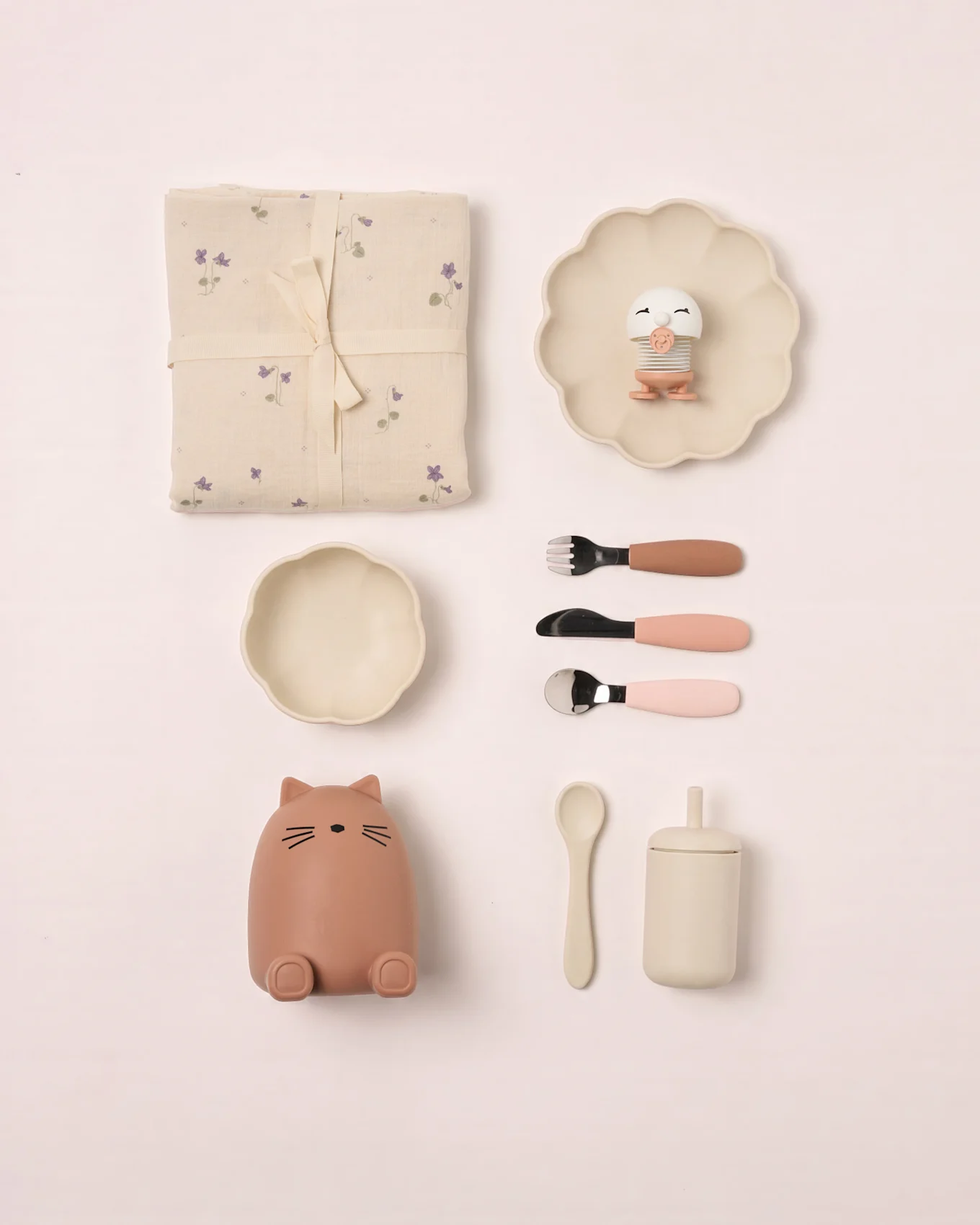 Conjunto bebé: manta floral, prato festonado, brinquedo pássaro, tigela, recipiente gato, talheres, colher e copo com tampa.