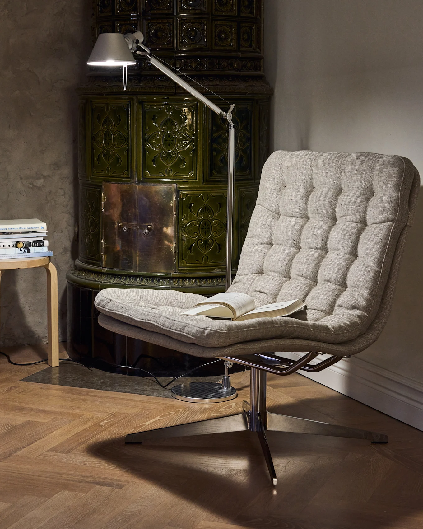 Aconchegante canto de leitura com poltrona estofada, candeeiro de pé ajustável e fogão de azulejos verde escuro.