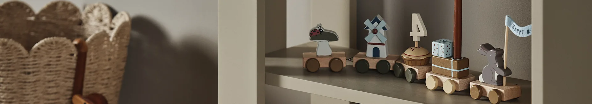 Um comboio de brinquedo de madeira numa prateleira, com carruagens que exibem uma joaninha, moinho de vento, cupcake com vela '4', presente e um coelhinho com uma bandeira "Happy B".