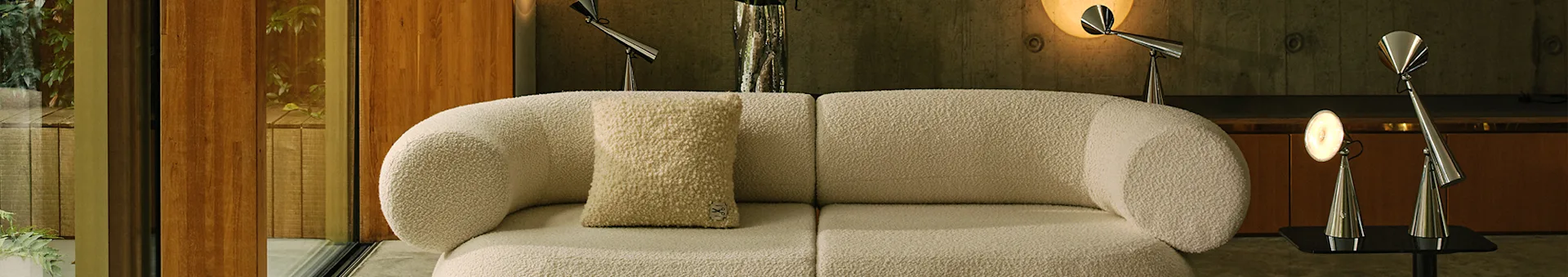 Sala de estar moderna com um sofá modular bouclé esbranquiçado, um tapete claro estampado e candeeiros de metal.
