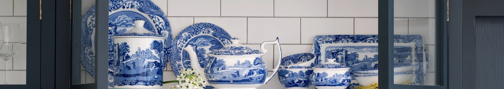 Serviço de jantar de porcelana azul e branca com padrões, incluindo bule, pratos e taças, num armário azul-escuro.