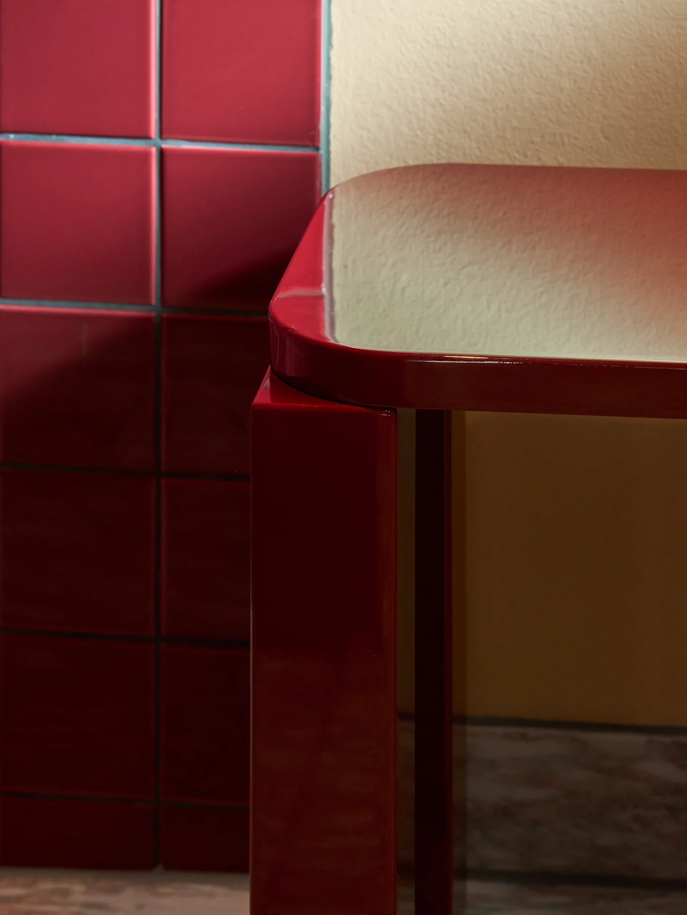 Elegante e brilhante banco retangular vermelho com bordas arredondadas sobre piso de mármore, junto a uma parede de azulejos vermelhos.