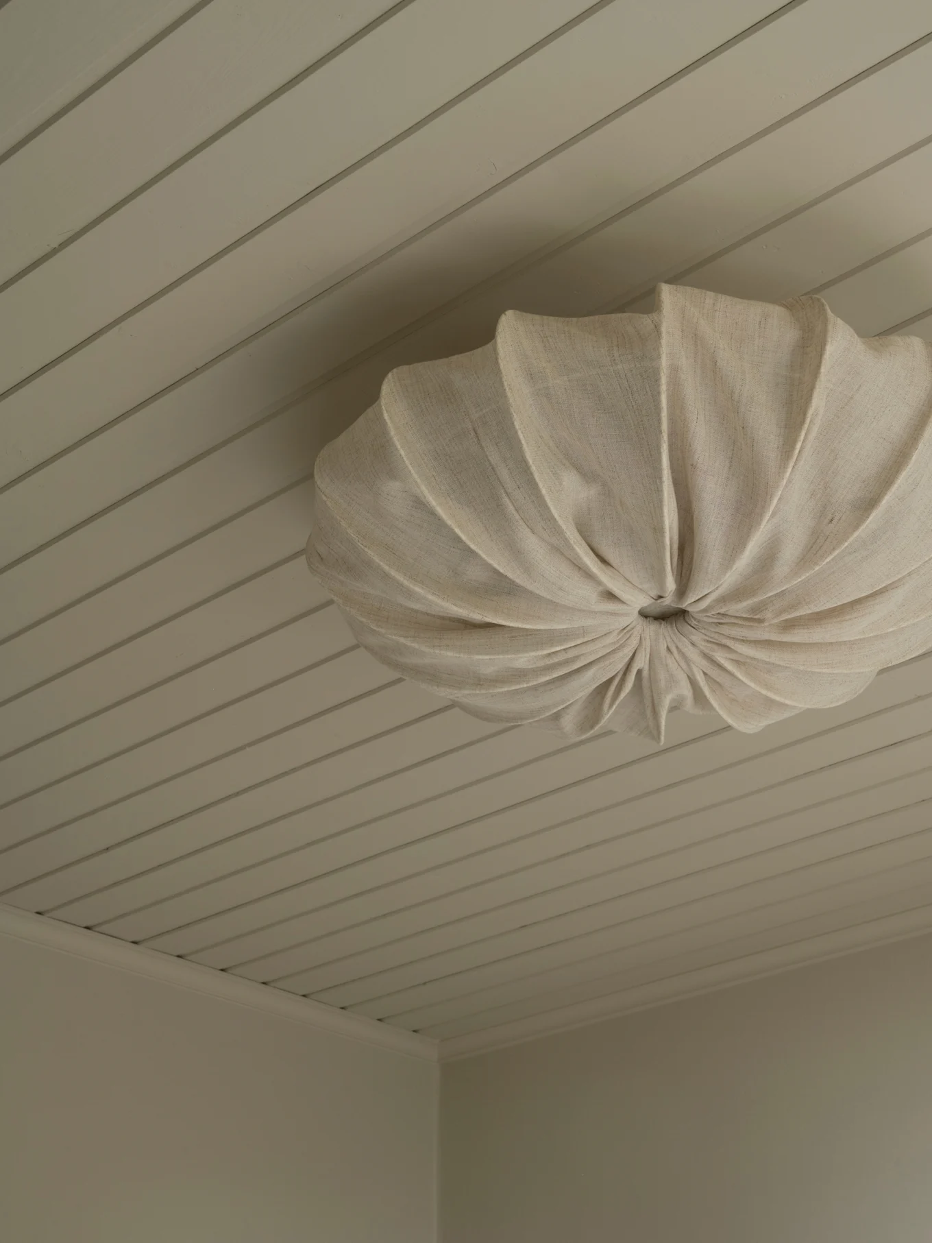 Uma luminária de teto de tecido plissado creme montada em um teto de painéis claros.