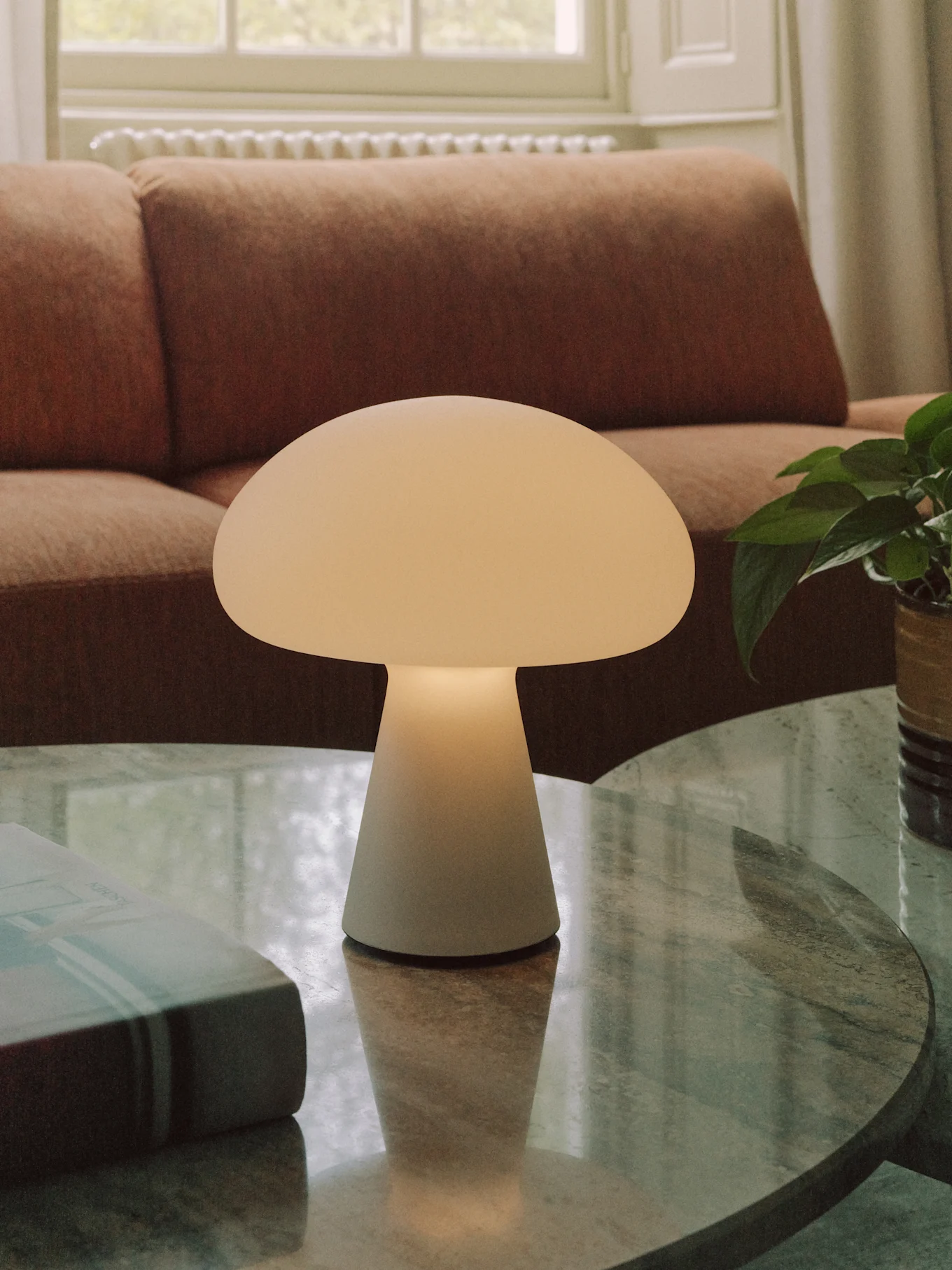 Um candeeiro de mesa em forma de cogumelo branco-sujo numa mesa de centro redonda de mármore numa sala de estar.