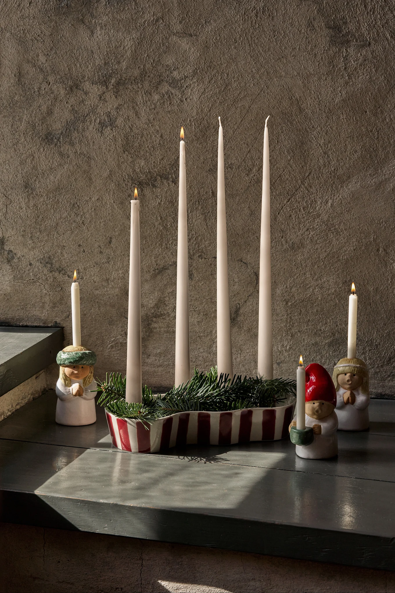 Decoração de Advento com quatro velas apagadas, pinho verde e três figuras com velas acesas.