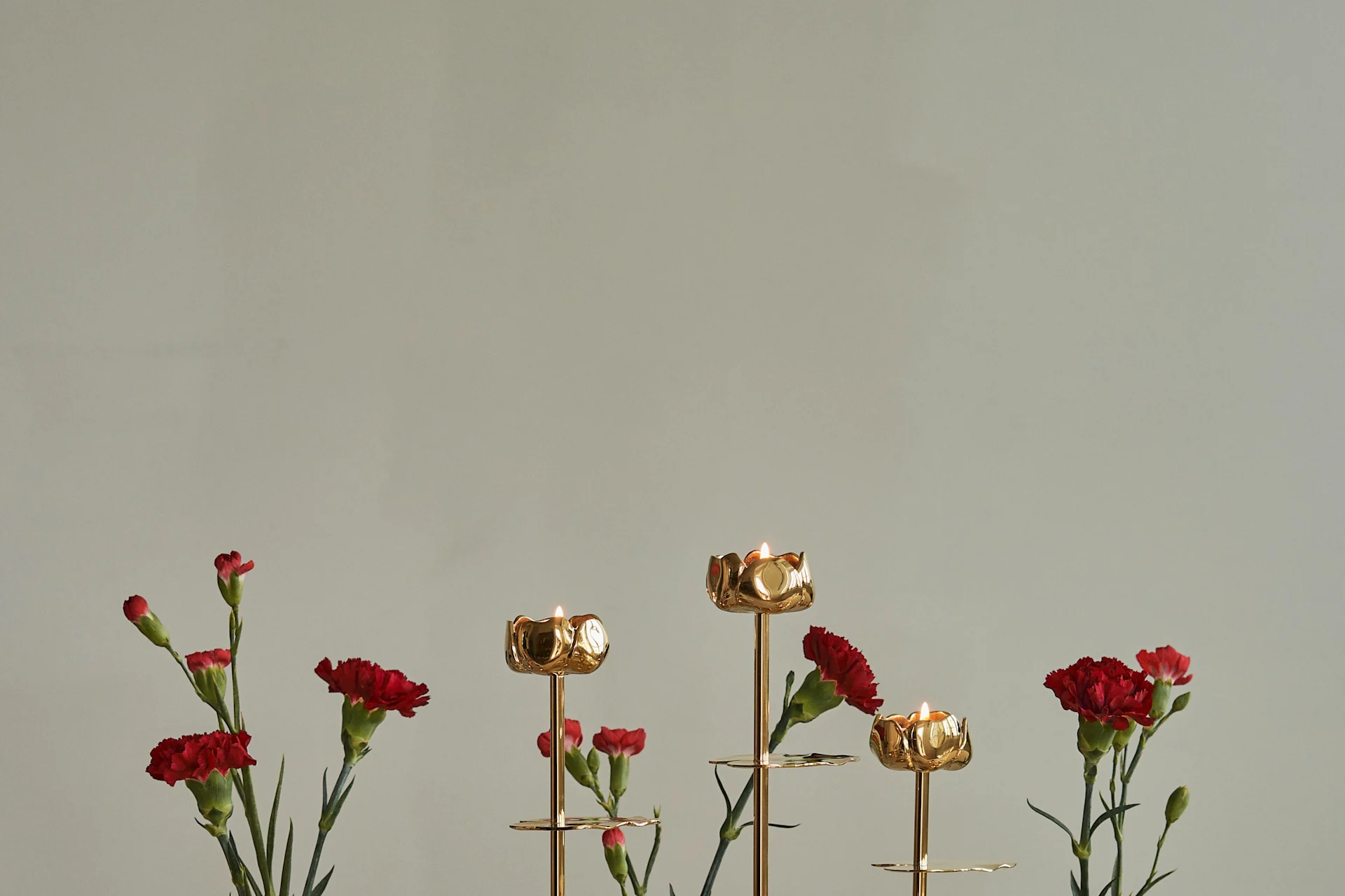 Castiçais dourados em forma de flor com velas acesas e cravos vermelhos.