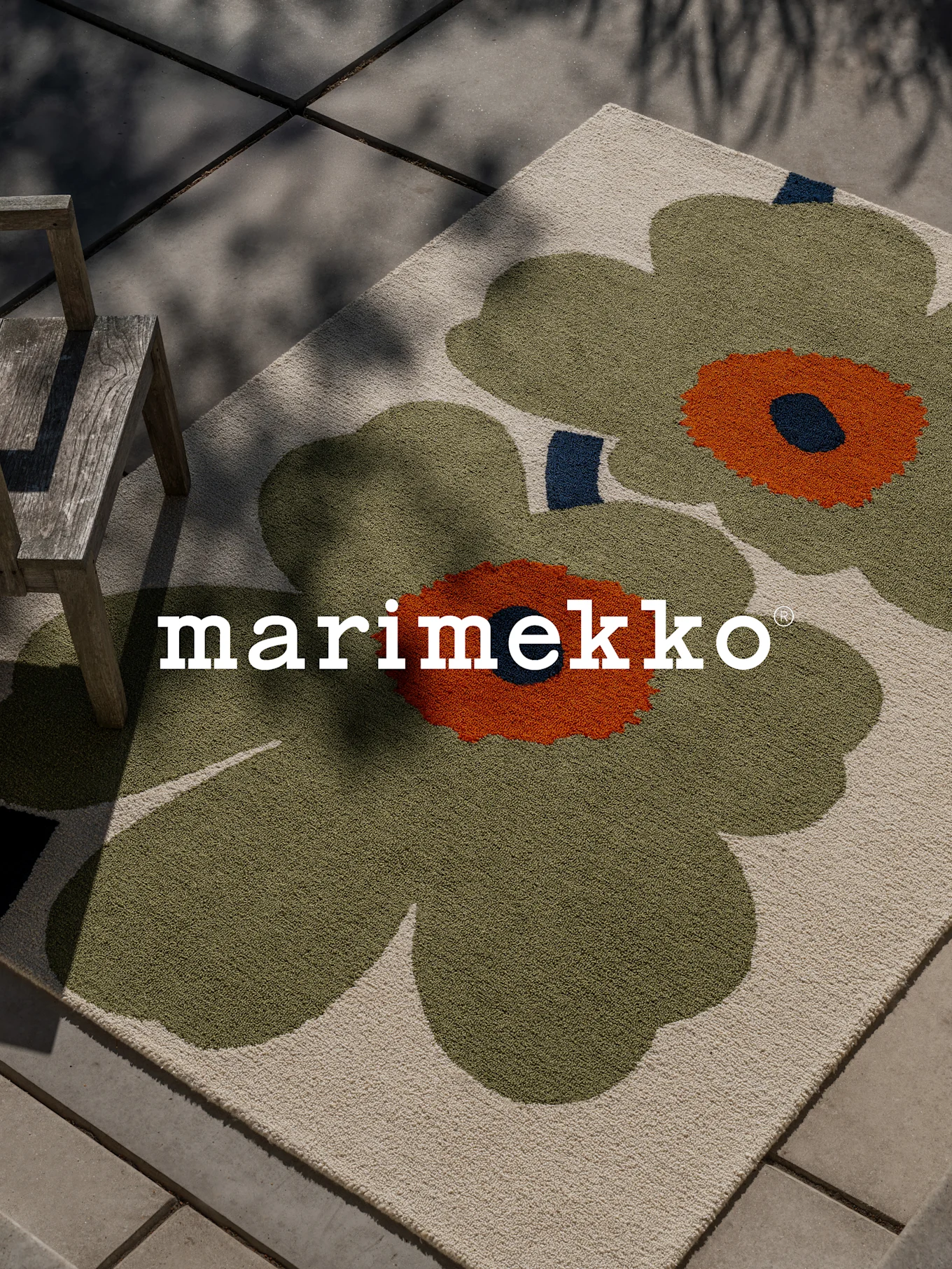 Tapete Marimekko com grande padrão floral verde e laranja num pátio com uma cadeira de madeira.